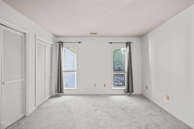 unfurnished bedroom with carpet flooring, a textured ceiling, baseboards, visible vents, and two closets