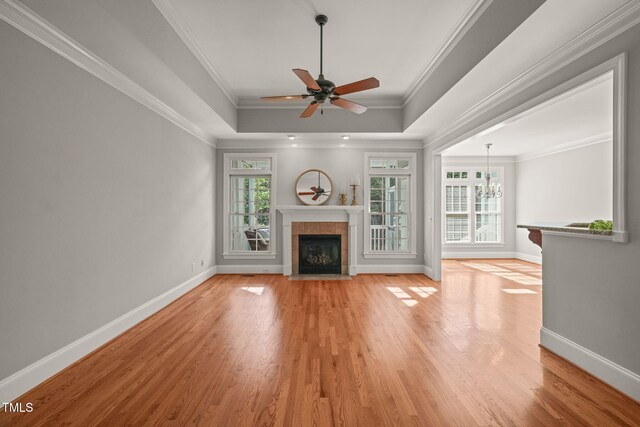 unfurnished living room with plenty of natural light, light wood-type flooring, baseboards, a raised ceiling, and crown molding