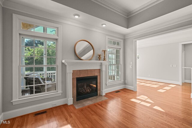 living room featuring wood finished floors, a tile fireplace, plenty of natural light, baseboards, and ornamental molding