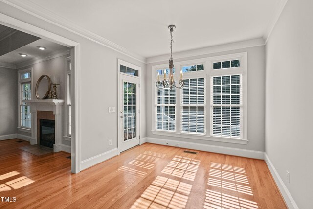 unfurnished dining area featuring a chandelier, ornamental molding, wood finished floors, baseboards, and a fireplace with flush hearth