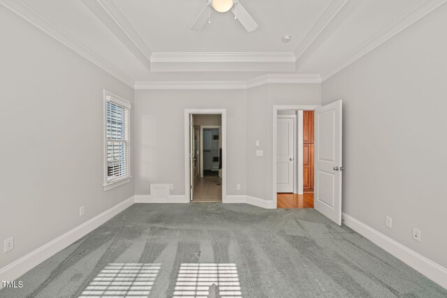 unfurnished bedroom with a raised ceiling, carpet flooring, ornamental molding, baseboards, and ceiling fan