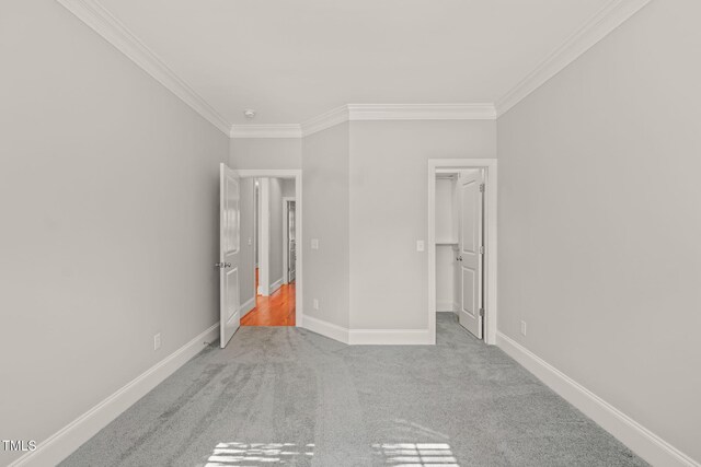 unfurnished bedroom featuring crown molding, carpet floors, baseboards, and a walk in closet