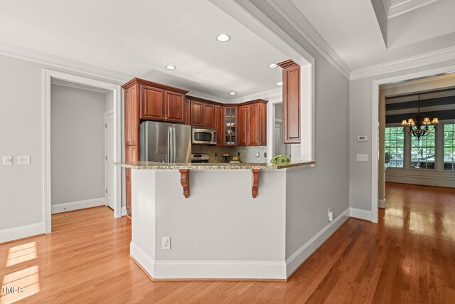 kitchen featuring appliances with stainless steel finishes, a kitchen breakfast bar, a chandelier, light stone counters, and tasteful backsplash