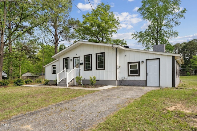 view of front of house with board and batten siding, a chimney, aphalt driveway, and a front yard