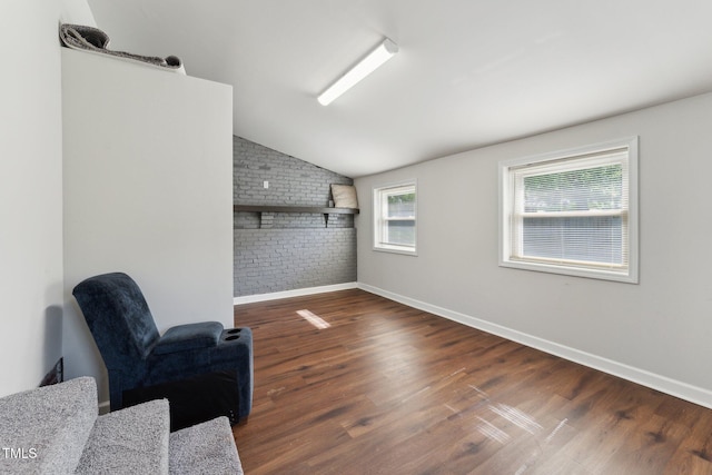 living area featuring brick wall, baseboards, vaulted ceiling, and wood finished floors