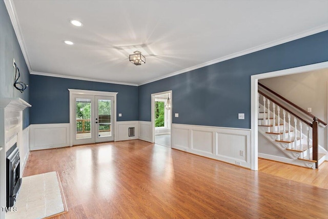 unfurnished living room with stairs, wood finished floors, ornamental molding, a fireplace, and wainscoting