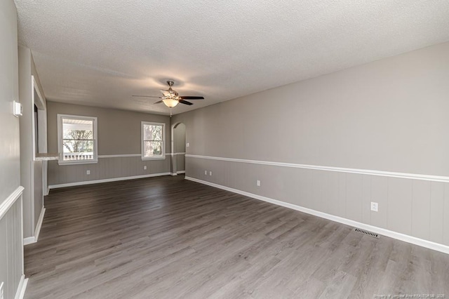 empty room with a textured ceiling, ceiling fan, arched walkways, and wood finished floors