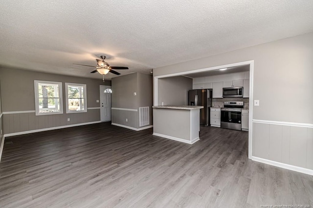 unfurnished living room featuring visible vents, wainscoting, ceiling fan, a textured ceiling, and dark wood finished floors
