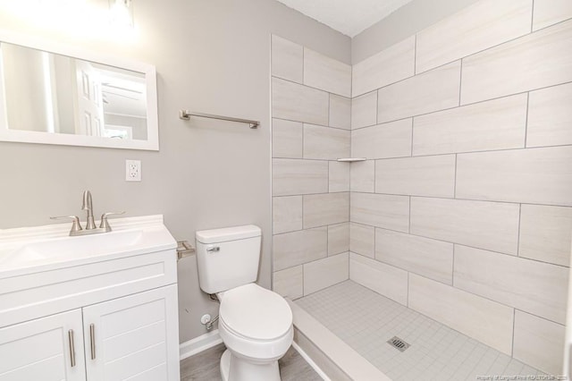 bathroom featuring vanity, baseboards, a tile shower, and toilet