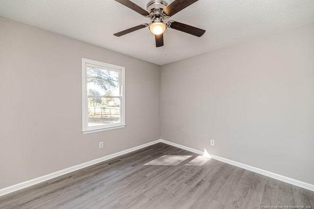 empty room featuring ceiling fan, baseboards, visible vents, and wood finished floors