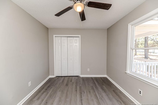unfurnished bedroom with a textured ceiling, baseboards, wood finished floors, and a closet
