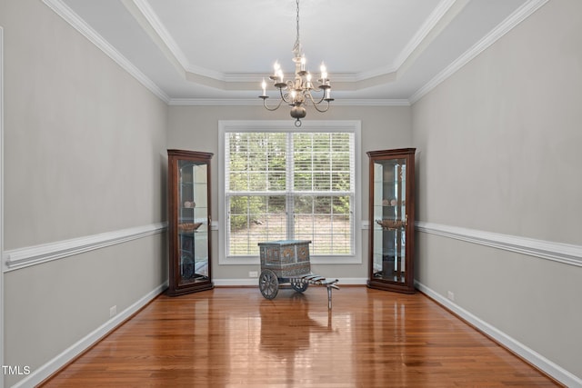 interior space featuring a raised ceiling, crown molding, wood finished floors, and a notable chandelier