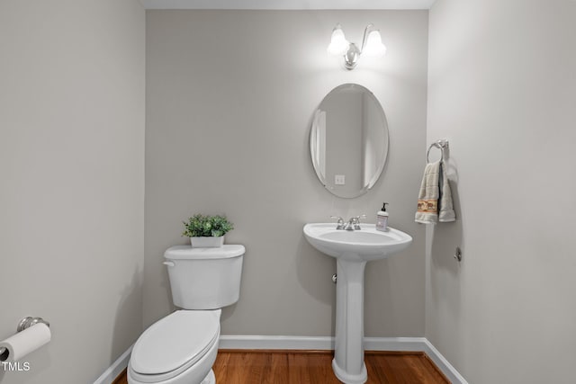 half bathroom featuring baseboards, a sink, toilet, and wood finished floors