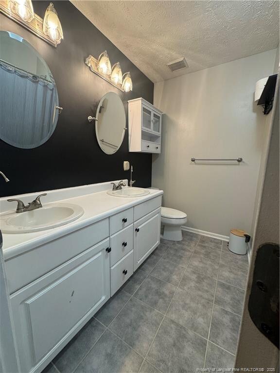 5870 Mcdonald Rd, Parkton, NC 28371 - bathroom featuring a sink, double vanity, a textured ceiling, and visible vents