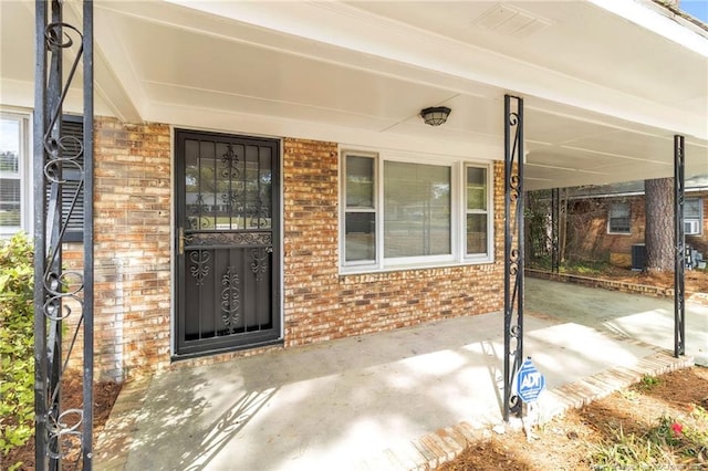 property entrance featuring brick siding, covered porch, and central air condition unit