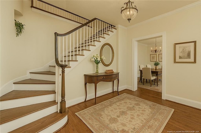 entrance foyer with ornamental molding, stairs, a notable chandelier, and wood finished floors