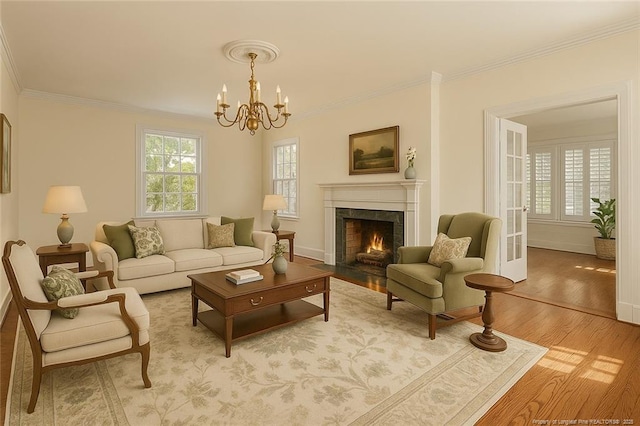 living room with an inviting chandelier, wood finished floors, a fireplace with flush hearth, crown molding, and baseboards