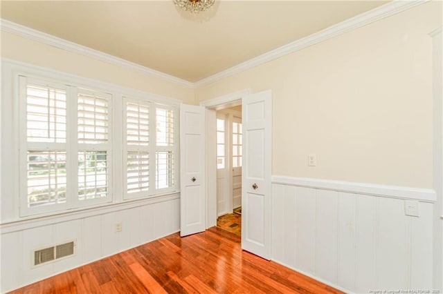 empty room featuring crown molding, a wainscoted wall, visible vents, and wood finished floors