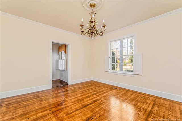 spare room with an inviting chandelier, wood finished floors, baseboards, and crown molding