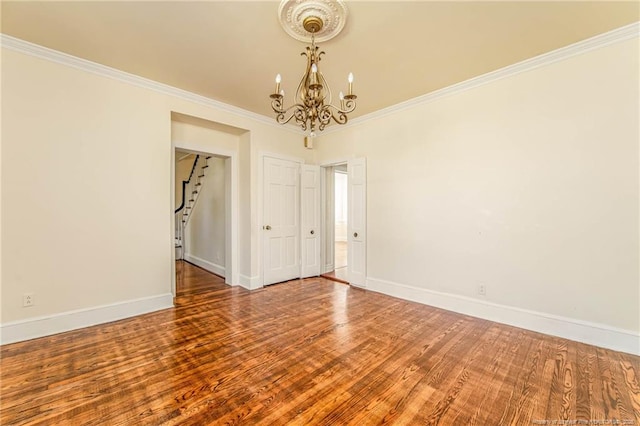 spare room with crown molding, wood finished floors, baseboards, and a notable chandelier