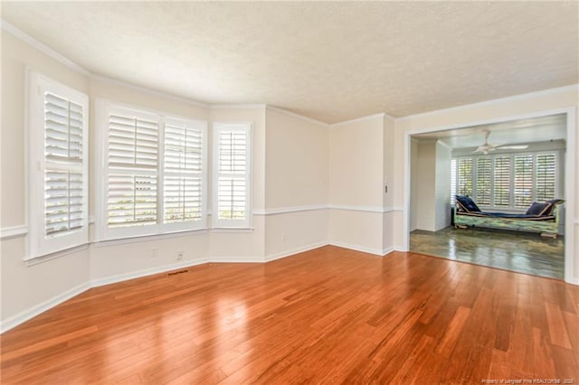 spare room featuring wood finished floors, a ceiling fan, a textured ceiling, baseboards, and ornamental molding
