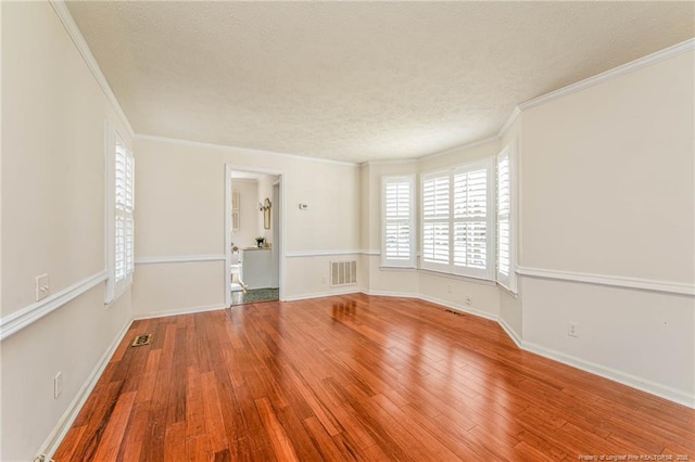 unfurnished room with ornamental molding, wood-type flooring, visible vents, and a textured ceiling