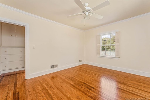 empty room with crown molding, wood finished floors, visible vents, and baseboards