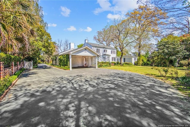 view of front of house with aphalt driveway, a carport, a chimney, and a front yard
