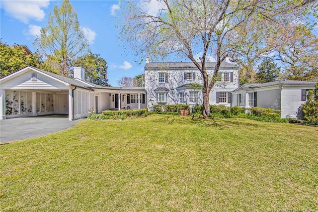 view of front of house with aphalt driveway, an attached carport, a chimney, and a front yard