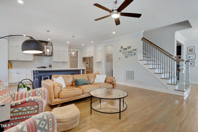 living room with visible vents, ornamental molding, stairway, light wood-type flooring, and a ceiling fan
