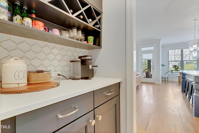 bar featuring an inviting chandelier, baseboards, light wood finished floors, backsplash, and decorative light fixtures
