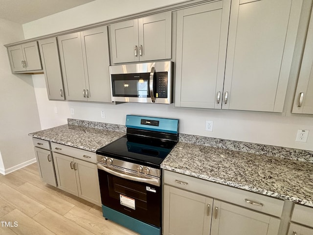 76 Commons Cir, Clayton, NC 27520 - kitchen featuring appliances with stainless steel finishes, gray cabinetry, light stone countertops, baseboards, and light wood-type flooring