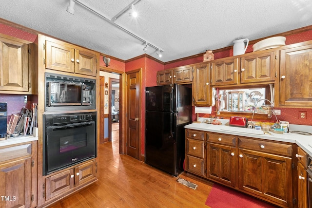 kitchen featuring a textured ceiling, light countertops, black appliances, and light wood-type flooring