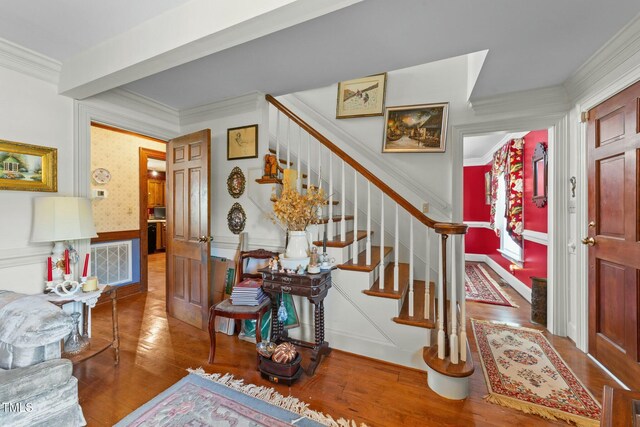 entryway with a wainscoted wall, stairs, wood finished floors, visible vents, and ornamental molding