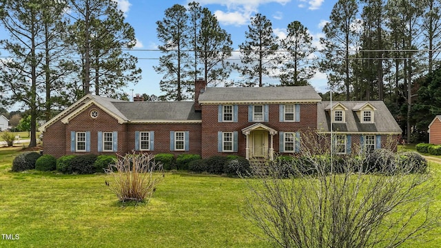 view of front facade with a chimney, a front lawn, and brick siding