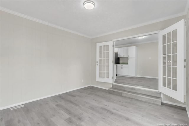 spare room with light wood-type flooring, french doors, ornamental molding, baseboards, and visible vents