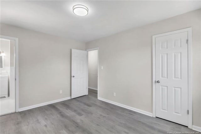 unfurnished bedroom featuring ensuite bathroom, baseboards, and wood finished floors