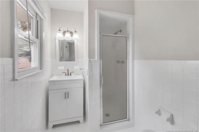 bathroom with a wainscoted wall, vanity, a stall shower, and tile walls
