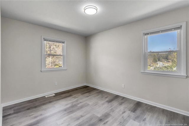 unfurnished room featuring visible vents, baseboards, and wood finished floors