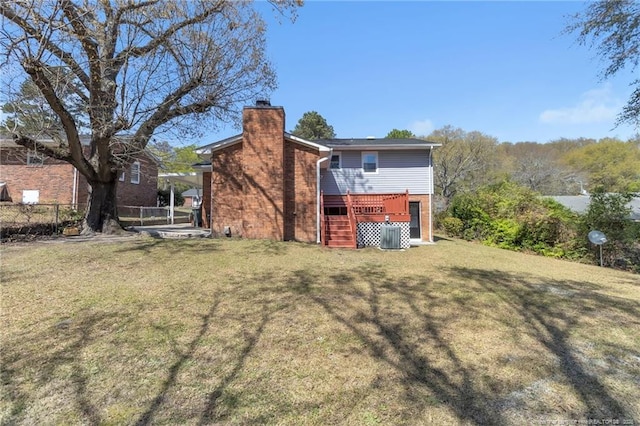 back of property with a chimney, a wooden deck, fence, brick siding, and a lawn