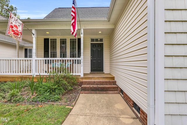 view of exterior entry with a shingled roof and a porch