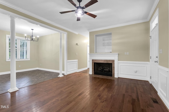 unfurnished living room featuring ceiling fan with notable chandelier, ornate columns, a premium fireplace, crown molding, and dark wood finished floors