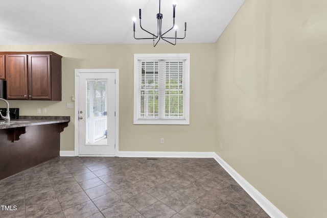 unfurnished dining area featuring baseboards, a chandelier, and a sink