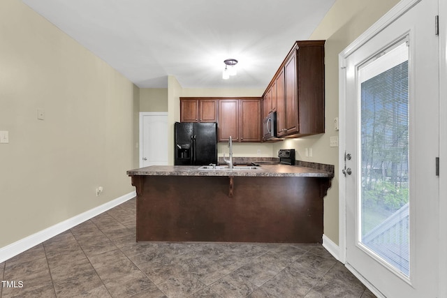 kitchen with a sink, a peninsula, black appliances, baseboards, and dark countertops