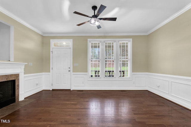 unfurnished living room with a ceiling fan, crown molding, dark wood finished floors, wainscoting, and a high end fireplace