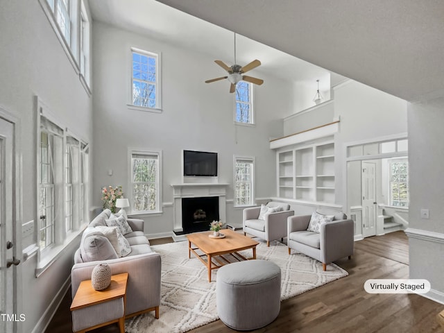 living room with baseboards, wood finished floors, a fireplace with raised hearth, and a ceiling fan