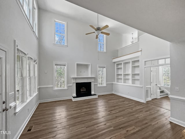 unfurnished living room with a ceiling fan, a fireplace with raised hearth, baseboards, and wood finished floors