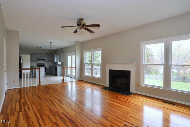 3313 Sparrowhawk Dr, High Point, NC 27265 - unfurnished living room with visible vents, baseboards, light wood-style floors, a fireplace with flush hearth, and ceiling fan with notable chandelier