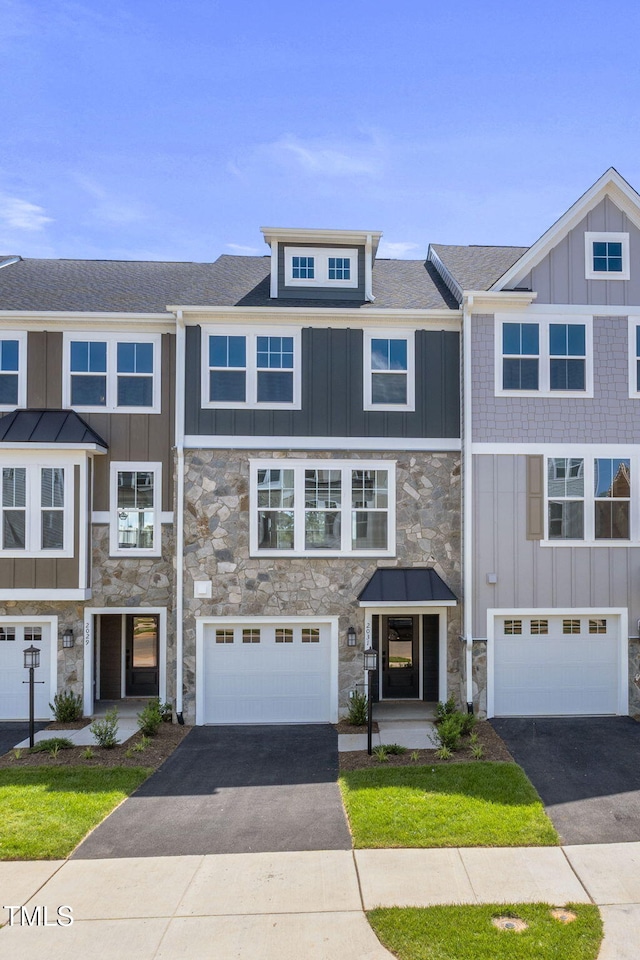 townhome / multi-family property with stone siding, board and batten siding, driveway, and an attached garage