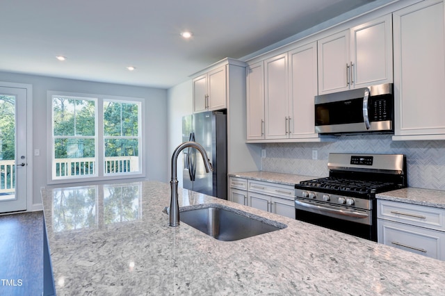 kitchen with light stone countertops, stainless steel appliances, recessed lighting, tasteful backsplash, and a sink